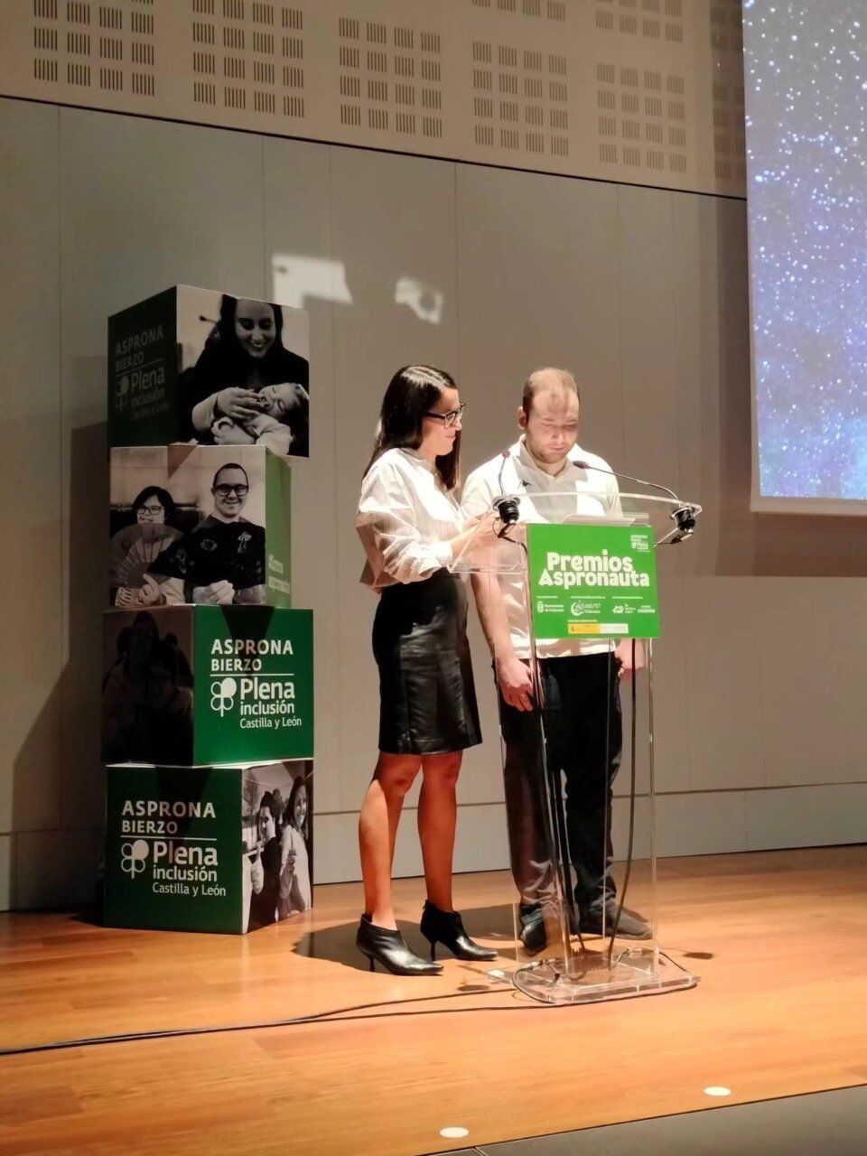 Dos personas frente a un atril con el rótulo Premios Aspronauta en un escenario.