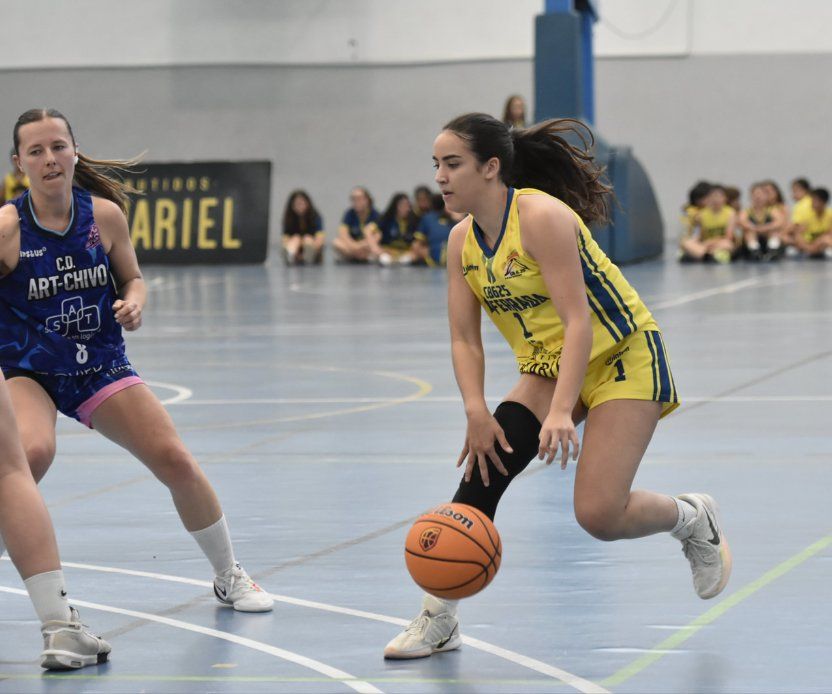 Una jugadora de amarillo bota el balón mientras otra de azul la defiende.