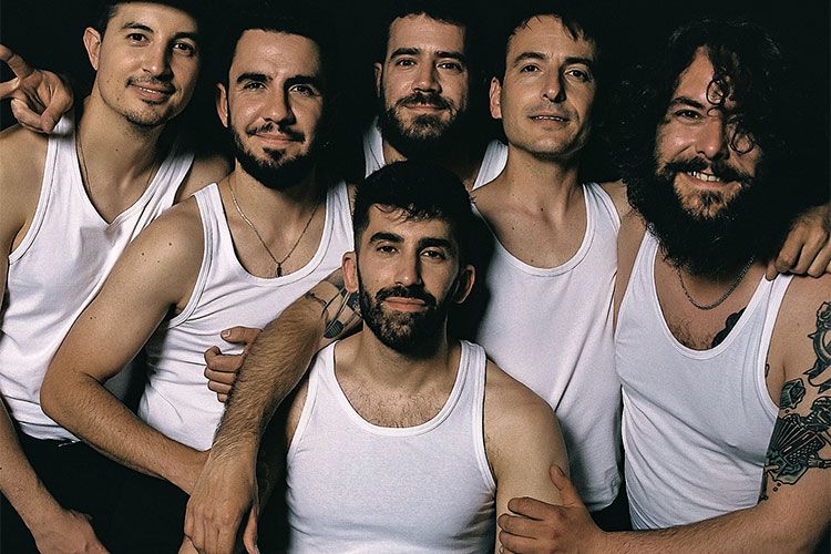 Seis hombres posan juntos con camisetas blancas sobre un fondo oscuro.