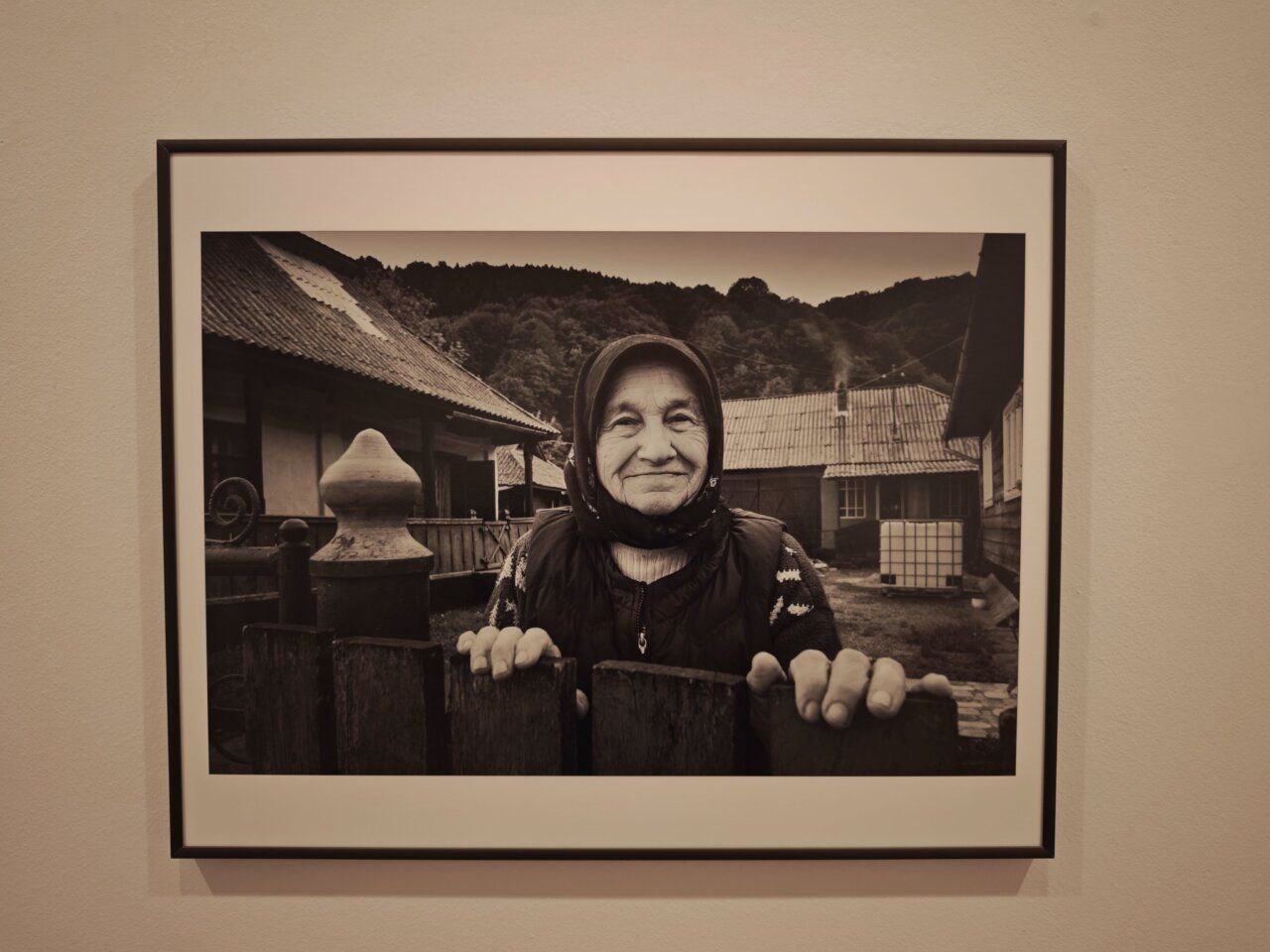 Retrato en blanco y negro de una mujer mayor sonriendo frente a una casa.