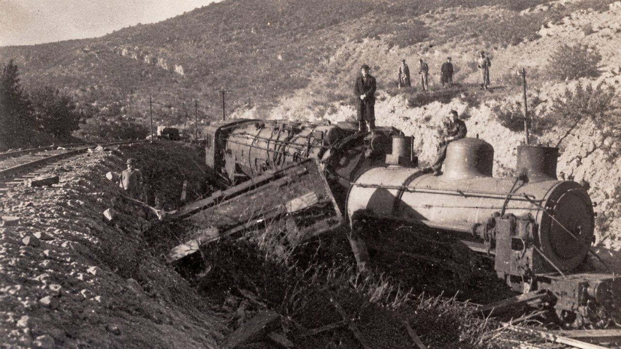 Fotografía en blanco y negro de locomotoras descarriladas y personas en una ladera rocosa