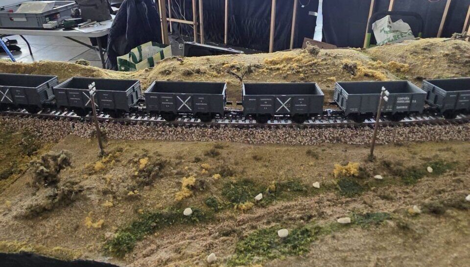 Maqueta ferroviaria con vagones de mercancías sobre una vía entre paisaje modelado