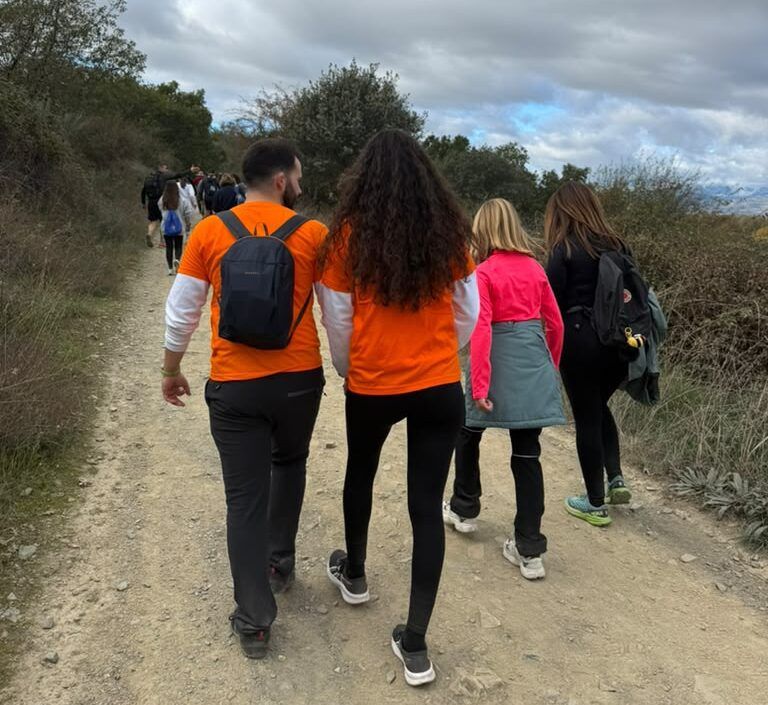 Varias personas caminan por un sendero, algunas con camisetas naranjas y mochilas.