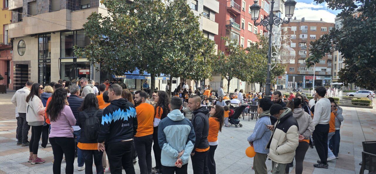 Grupo de personas reunido en una plaza urbana, con varios asistentes vestidos de naranja.