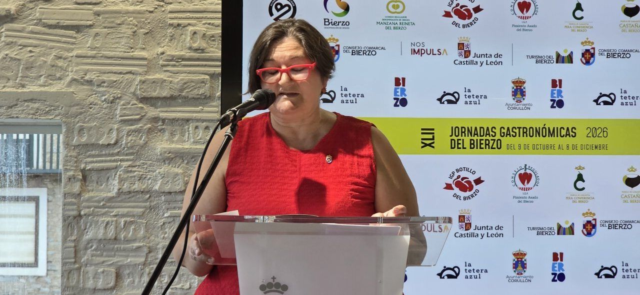 Mujer con vestido rojo habla ante un atril frente al panel de las Jornadas del Bierzo