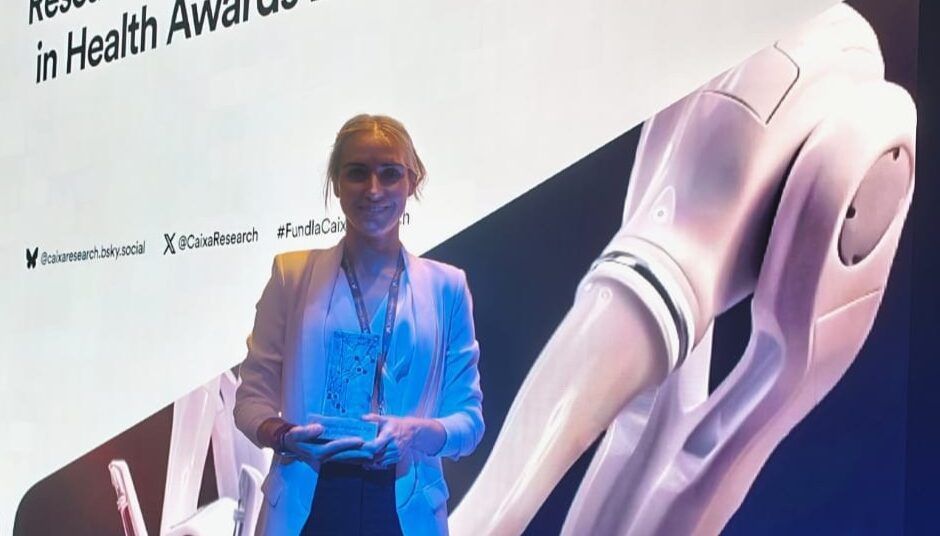Mujer sostiene una placa frente al escenario de los premios de investigación e innovación en salud 2026