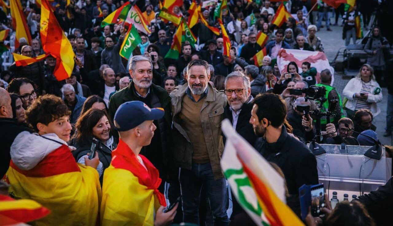 Multitud con banderas de España y VOX rodea a varios hombres en un acto público