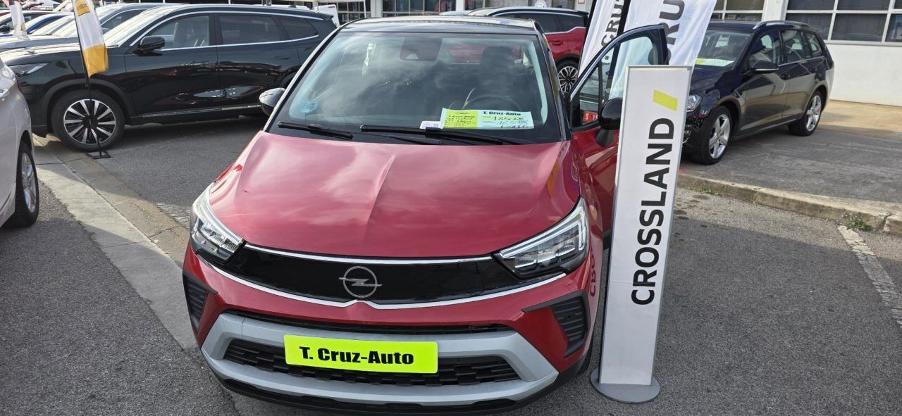 Opel Crossland rojo estacionado entre otros coches, junto a un cartel con su nombre.