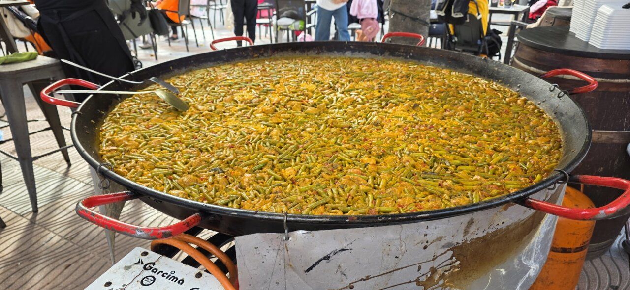 Una gran paellera llena de arroz y verduras ocupa el primer plano.