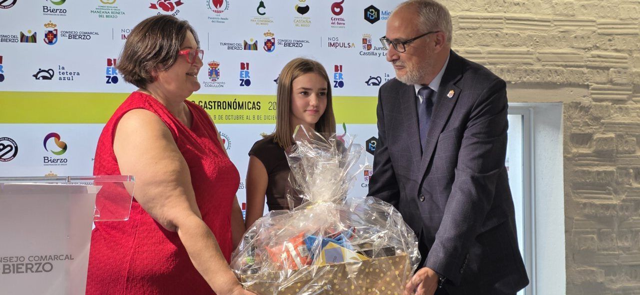 Tres personas posan junto a una cesta envuelta frente a un panel de las jornadas gastronómicas.