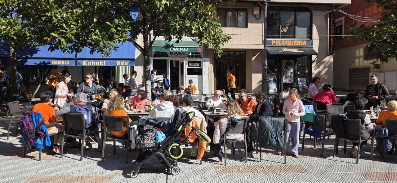 Personas sentadas en mesas de una terraza exterior bajo la sombra de árboles