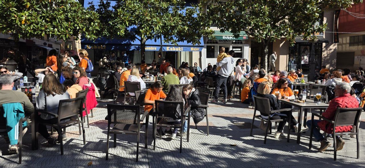 Personas sentadas en mesas de una terraza bajo los árboles.