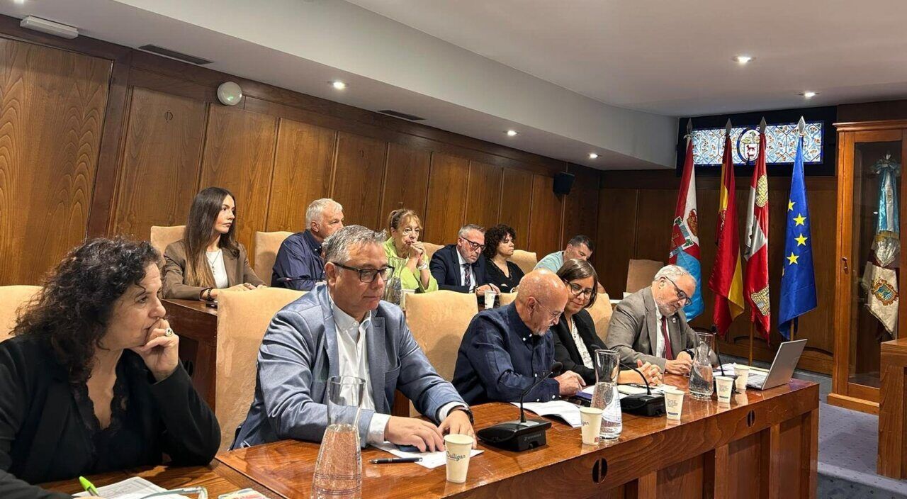 Personas sentadas alrededor de una mesa en una sala institucional con varias banderas.
