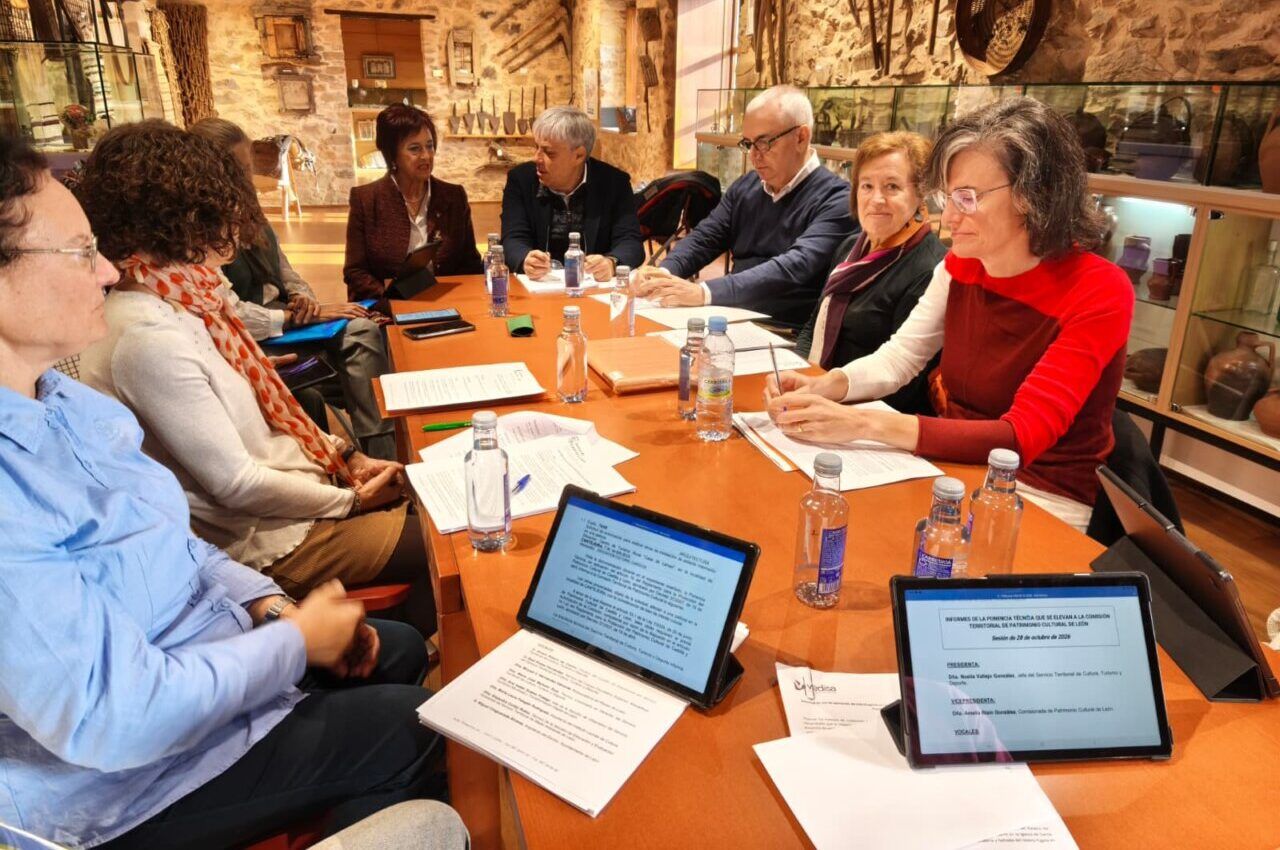 Personas reunidas alrededor de una mesa con documentos y tabletas en una sala de piedra.