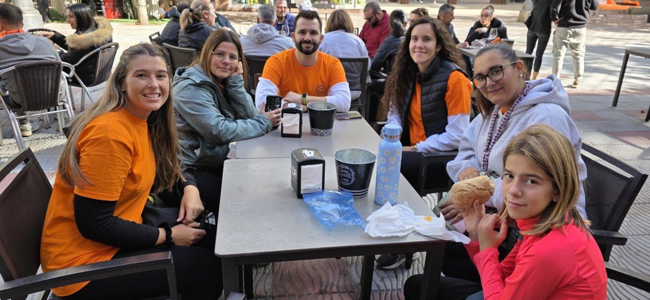Varias personas sentadas alrededor de una mesa al aire libre; algunas llevan camisetas naranjas.