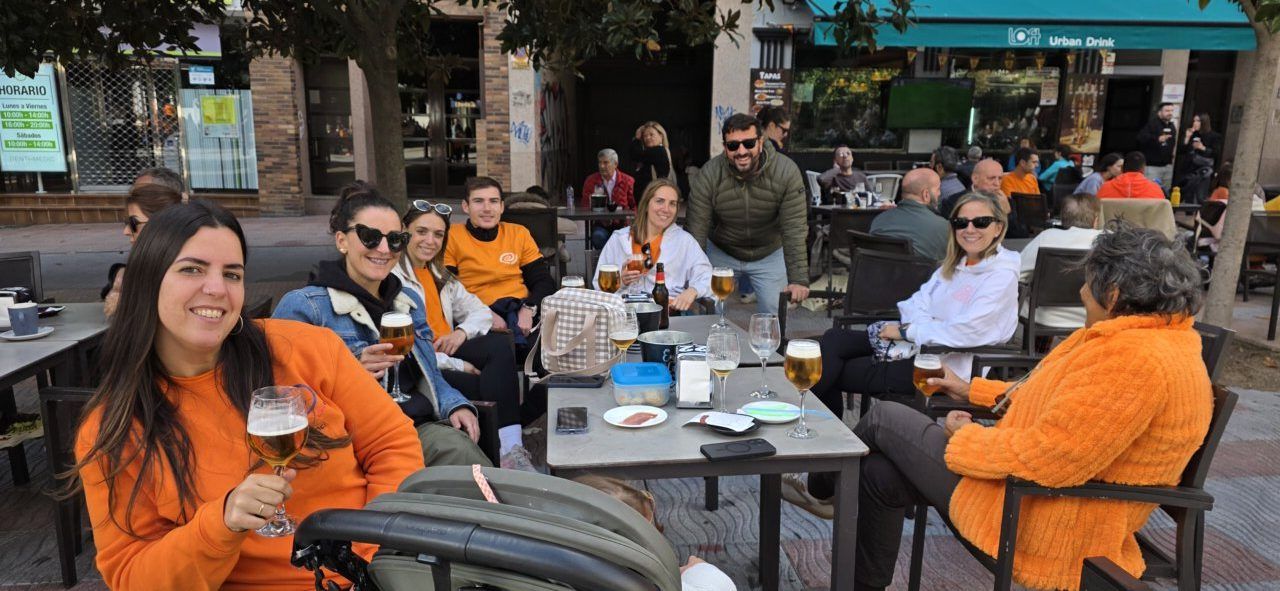 Personas sentadas alrededor de mesas en una terraza, con bebidas y un carrito infantil.