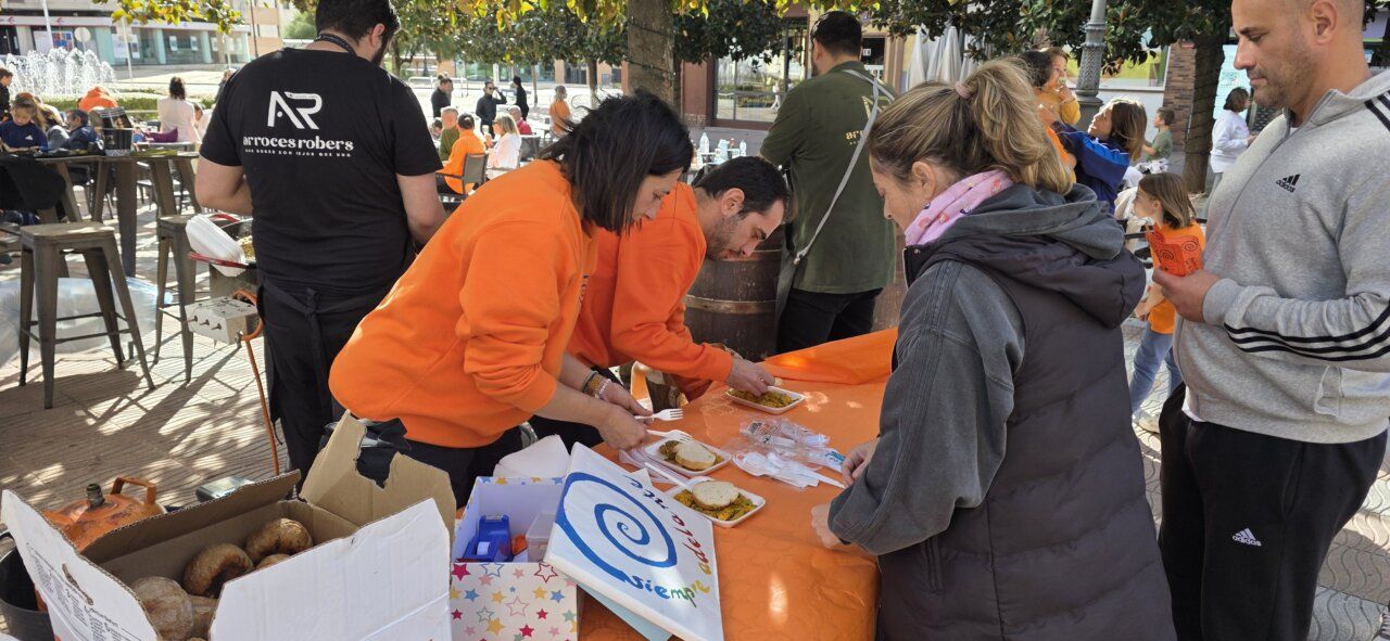 Personas sirven comida en una mesa al aire libre junto a una caja de pan.