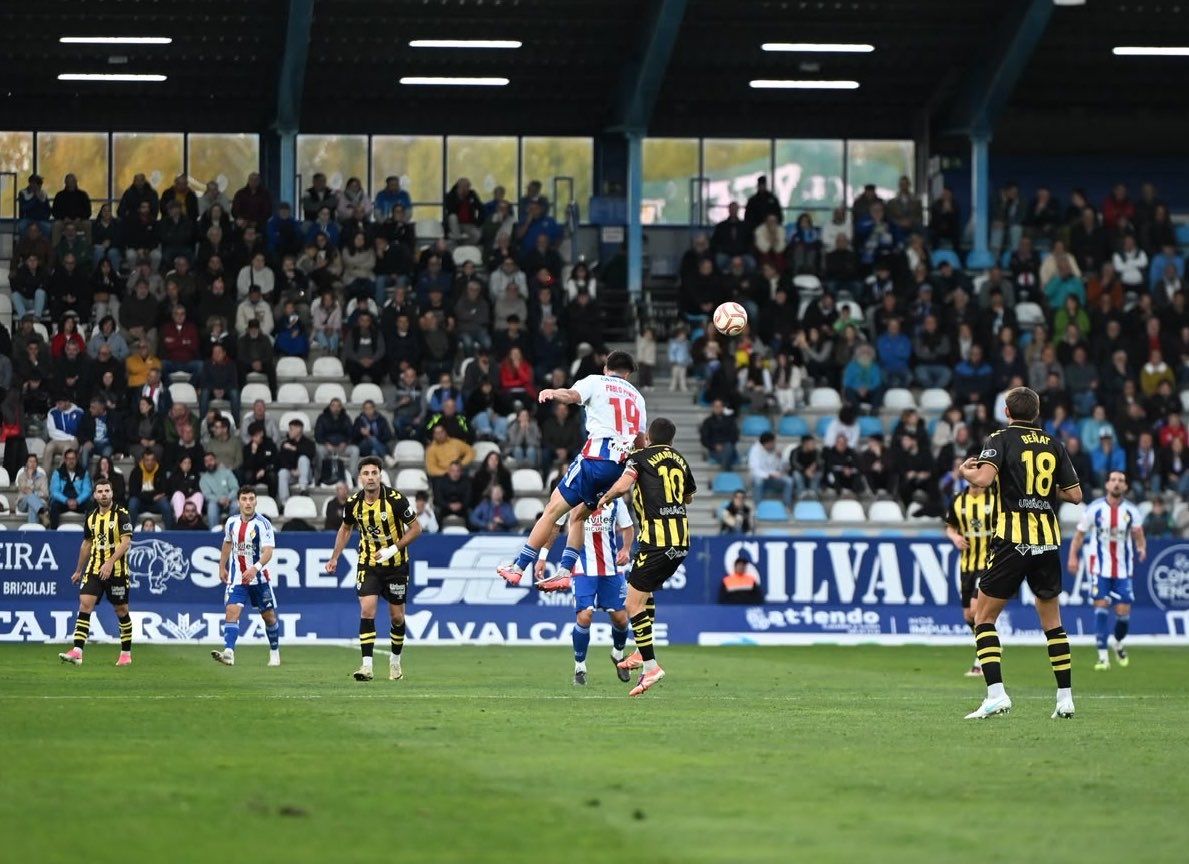 Futbolistas disputan un balón aéreo durante el partido ante las gradas