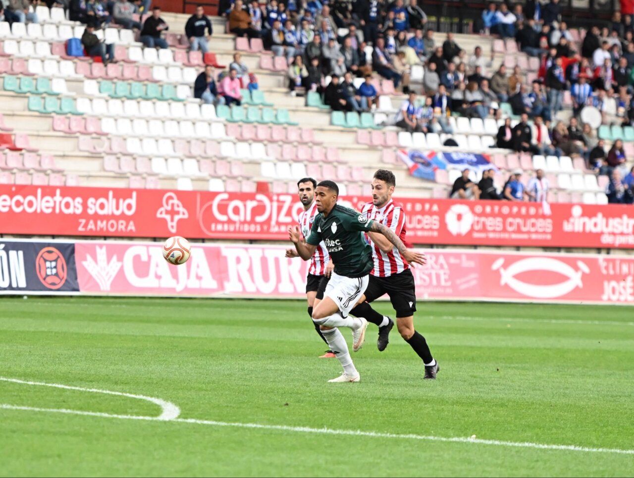 Futbolistas de verde y de camiseta rojiblanca disputan el balón sobre el césped.