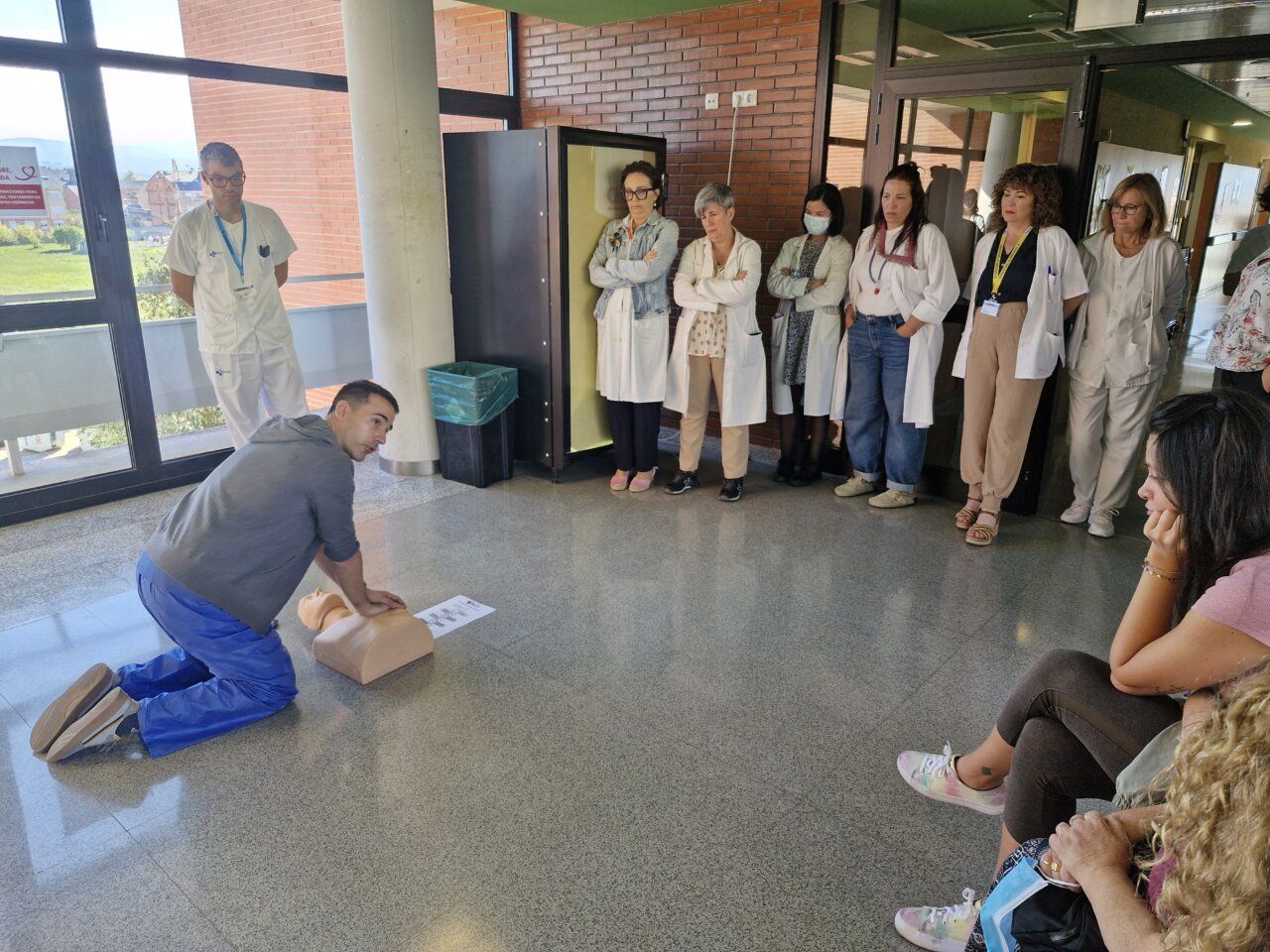 Un hombre practica compresiones torácicas en un maniquí mientras varias personas observan.