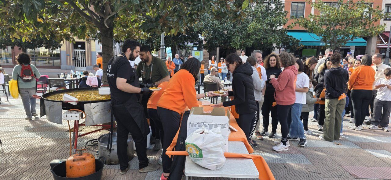Personas se sirven comida junto a una gran paellera en una plaza al aire libre