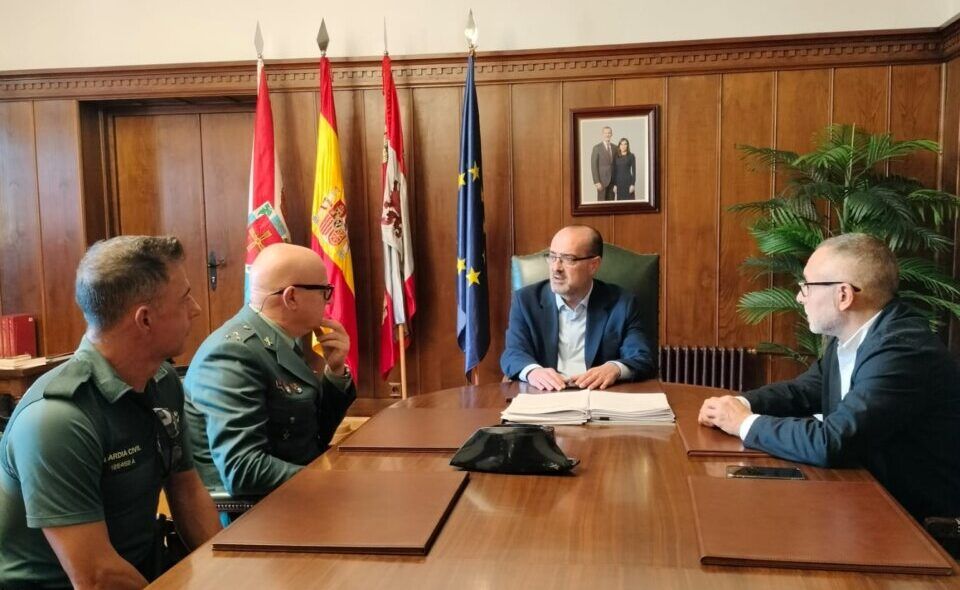 Cuatro hombres reunidos alrededor de una mesa, con banderas y dos agentes uniformados.