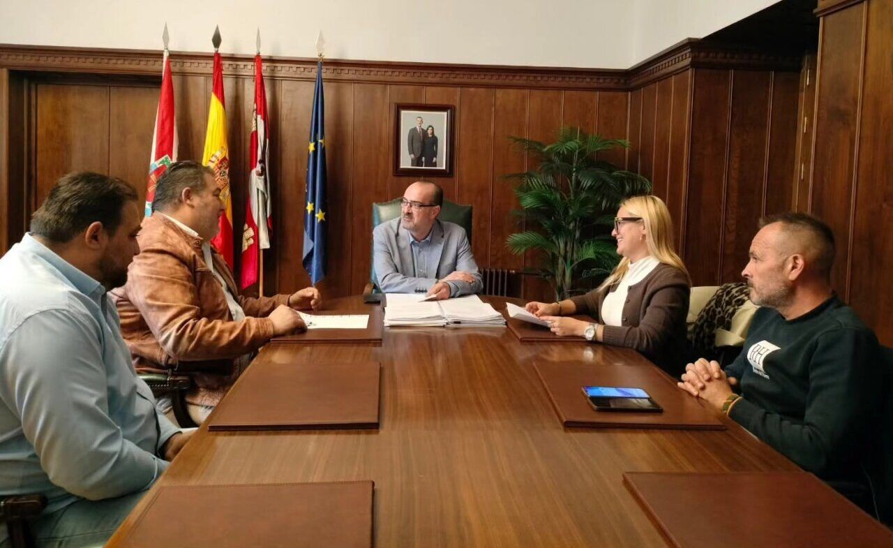 Varias personas conversan alrededor de una mesa en una sala con banderas.