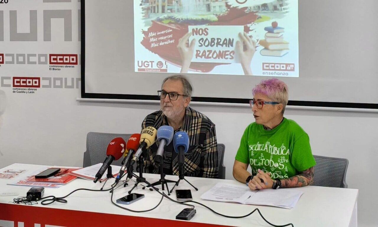 Dos personas ante micrófonos durante una rueda de prensa con un cartel de huelga docente proyectado