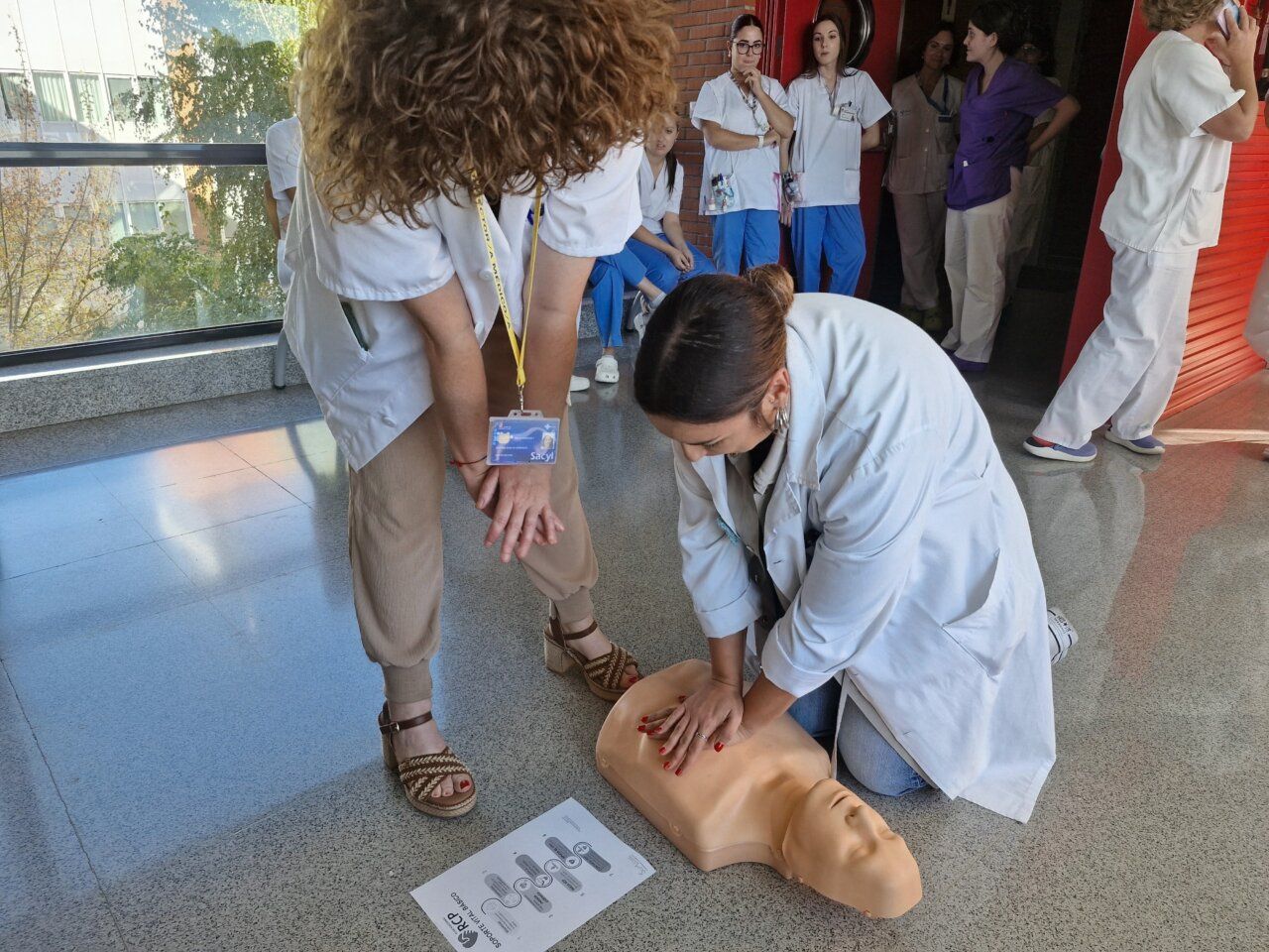 Una mujer practica compresiones torácicas sobre un maniquí mientras varias personas observan.