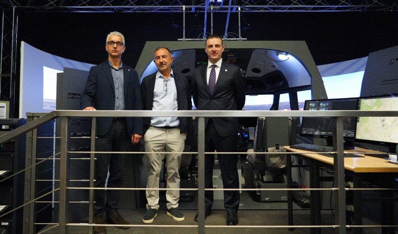 Tres hombres posan frente a un simulador de cabina rodeado de pantallas y controles