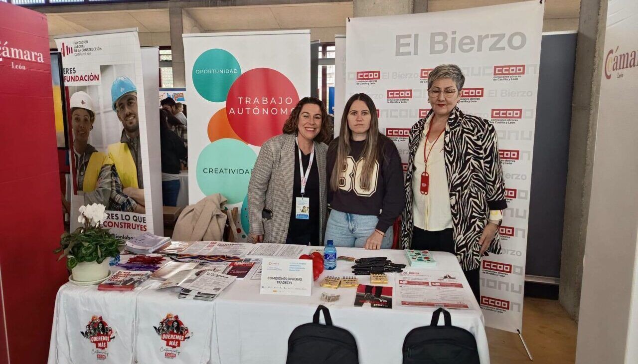Tres mujeres posan detrás de un puesto informativo con folletos, bolsas y carteles de El Bierzo y CCOO