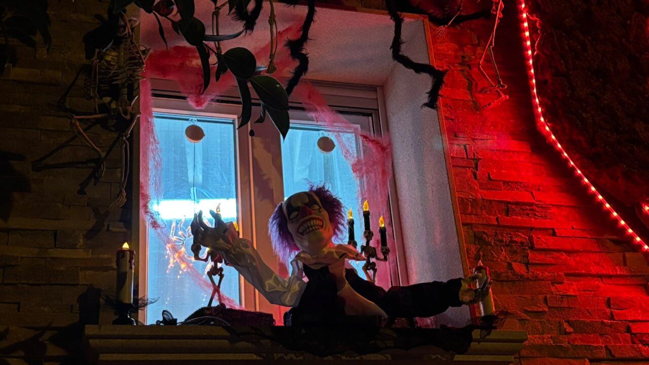 Decoración de Halloween en una ventana, con payaso siniestro, esqueletos y luces rojas.